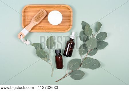 Essential Oils, Facial Creme Container And Massage Brush With Natural Eucalyptus Leaves On Green Bac