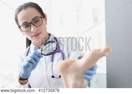 Woman Podiatrist Examining Heel Of Patient Using Magnifying Glass
