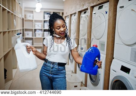 Cheerful African American Woman Hold Detergent Near Washing Machine In The Self-service Laundry.