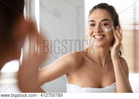 Woman Applying Cream Under Eyes Moisturizing Skin Posing In Bathroom
