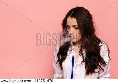 Young Woman Smokes A Hookah, Sheesha On A Pink Background. The Pleasure Of Smoking.