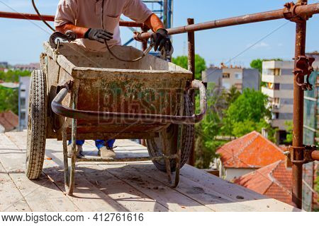 Construction Worker Is Attaching Crane Hooks To Industrial Tipping Barrow.