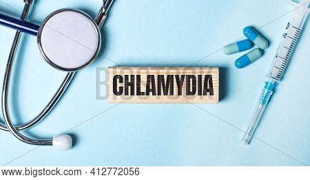 On A Blue Background, A Stethoscope, A Syringe And Pills And A Wooden Block With The Word Chlamydia.