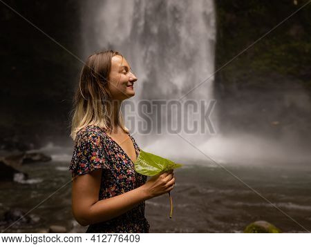 Caucasian Woman Holding Leaf, Enjoying Waterfall Landscape. Nature And Environment Concept. Travel L