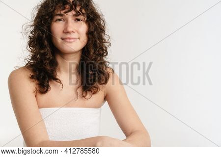 Half-naked woman looking at camera while posing in bath towel isolated over white background