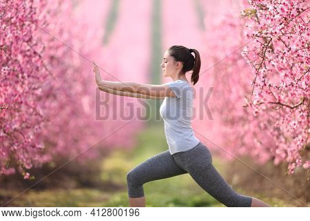 Side View Portrait Of A Woman Doing Tai Chi Exercise In A Pink Flowered Field