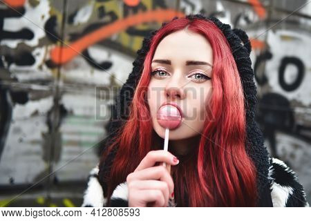 Portrait Of A Young Beauty In A Hoodie With A Delicious Pink Lollipop, Posing Against A Wall Of Graf