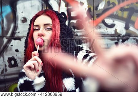 Portrait Of A Young Beauty In A Hoodie With A Delicious Pink Lollipop, Posing Against A Wall Of Graf