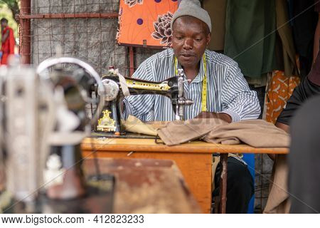 Tanzania, Masai Village - January 2020: Portrait Of Sewer Of Swiss Tailor Maasai Man Working With Se