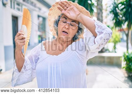 Middle age woman with grey hair using handfan on a very hot day of a heat wave