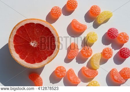 Slice Of Grapefruit And Sweet Fruit Hard Candies On White Table Background. Overhead View Of Colorfu