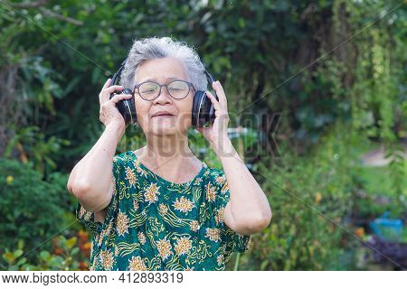 Senior Woman With Short Gray Hair Wearing Wireless Headphones Listening To A Favorite Song, Smiling 