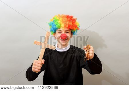 A Clown Dressed As A Catholic Pastor With A Cross And A Rosary. The Concept Of Blasphemy And Ridicul