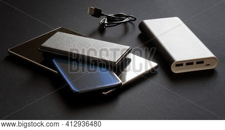 A Large And Capacious External Battery - Power Bank With Three Line Outputs Lies Next To Three Gadge