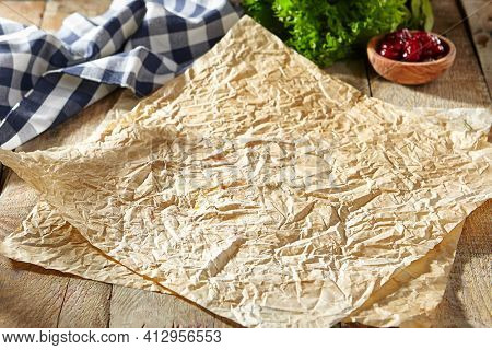 Baking paper with food ingredients. Wooden table at kitchen with baking utensil and fresh vegetables. Crumpled parchment or baking paper as a creative copy space