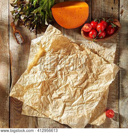 Baking paper with food ingredients. Wooden table at kitchen with baking utensil and fresh vegetables. Crumpled parchment or baking paper as a creative copy space. Top view