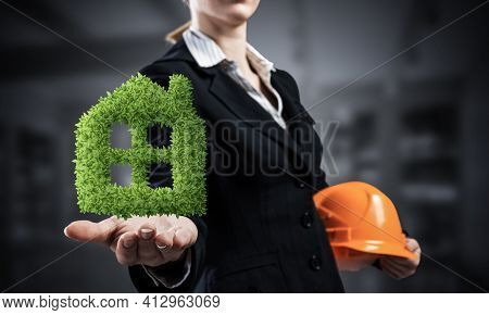 Real Estate Agent Holds In Palm Green Plant In Shape Of House. Woman In Business Suit With Safety He