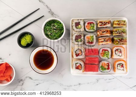 Various kinds of sushi placed on white square plate, seaweed salad and soy sauce in a bowl on the side. Asian food composition, top view.