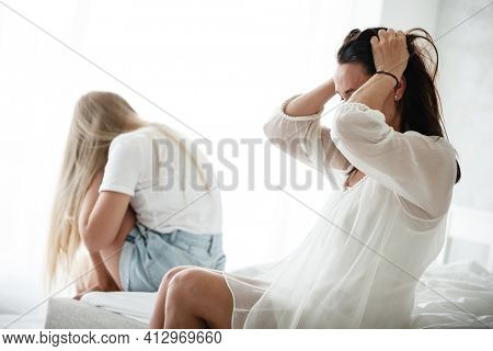 Family conflict and relations concept. Mother and daughter having quarrel and aguring at home. Sad woman and teenage girl sitting on bed. Not looking at each other