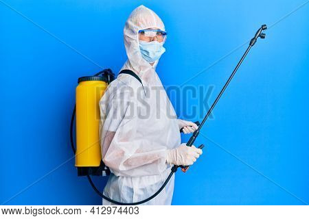 Covid specialist wearing decontamination protective suit and disinfectant spray, decontaminate and sanitize surface, standing over blue background