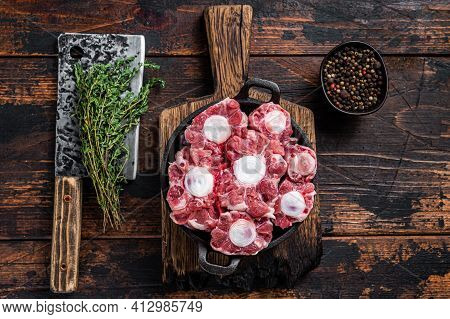Raw Veal Beef Oxtail Meat On Butcher Wooden Board With Cleaver. Dark Wooden Background. Top View