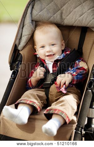 Cute little smiling baby in a baby carriage on the streets of the city. Smile of a  child sitting in a pram. A child laughs
