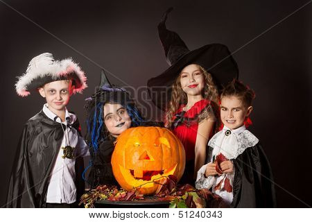 Cheerful children in halloween costumes posing with pumpkin. Over dark background.
