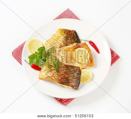 portion of baked carp meat with lemon and herb, served on a plate and linen with red square pattern