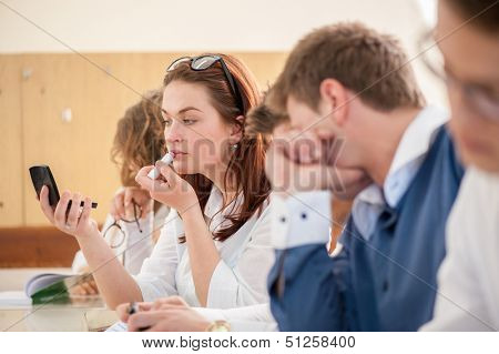 Schoolgirl putting a lipstick on her lips in a schoolroom