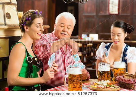 In Pub - friends in Tracht, Dirndl and Lederhosen drinking a fresh beer in Bavaria, Germany playing cards