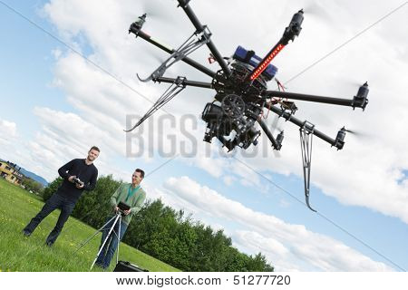 Young male engineers operating UAV helicopter against cloudy sky