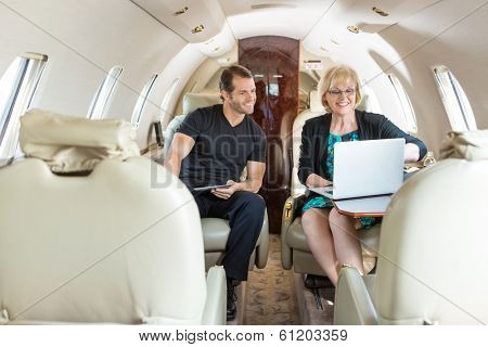 Business colleagues with laptop and digital tablet discussing on private jet