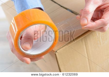 Hands with roll of transparent packaging, adhesive tape on a cardbox