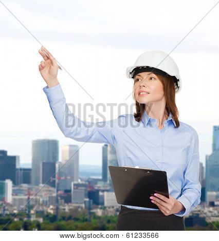 building, developing, consrtuction and architecture concept - smiling businesswoman in white helmet with clipboard pointing finger