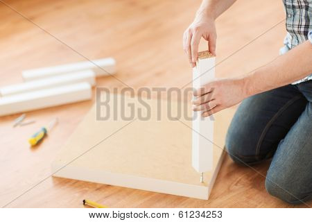 furniture, home and moving concept - close up of male hands assemblying legs to table