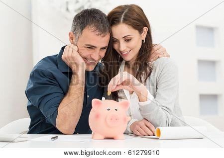 Portrait Of Happy Couple Inserting Coin In Piggybank