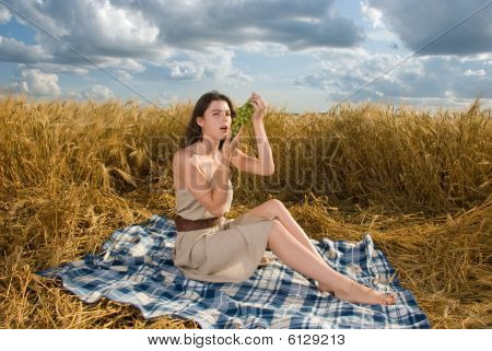 Hermosa chica en el picnic en el campo de trigo con uvas