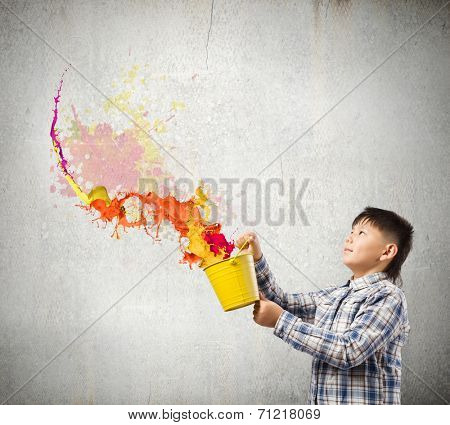 Young boy splashing colorful paint from bucket