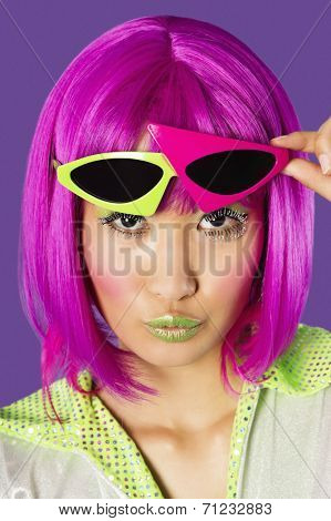 Portrait of young funky woman in pink wig puckering lips over purple background