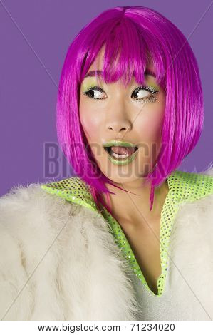 Surprised young funky woman in pink wig looking sideways over purple background