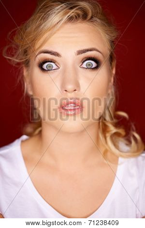 Beautiful young blond woman with a horrified expression looking at the camera with her eyes wide open in shock
