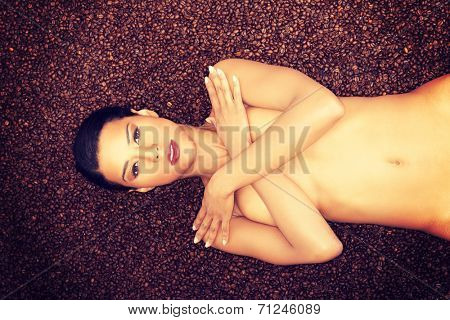 Attractive naked woman lying in coffee grains. Up front view.