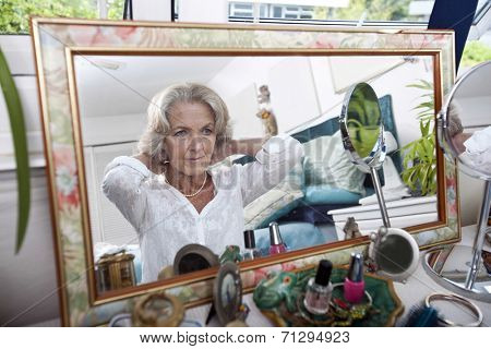 Mirror reflection of senior woman putting on necklace at home
