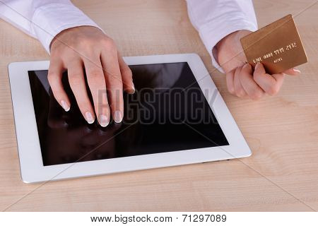 Female hands holding credit card and computer tablet on table close up