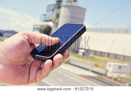 closeup of the hand of a man using a smartphone in an industrial park