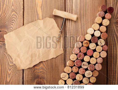 Wine bottle shaped corks, corkscrew and piece of paper for copy space over rustic wooden table background. Top view