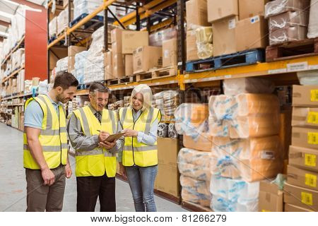 Manager writing on clipboard talking to colleague in a large warehouse