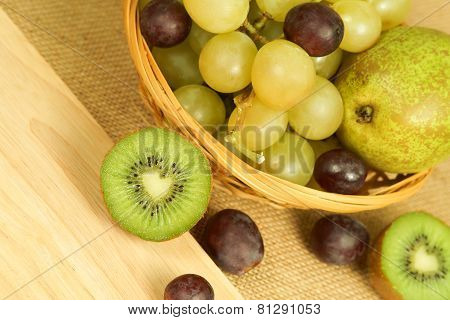 Cutted green kiwi on the board and fruits basket