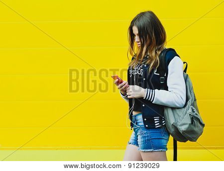 Happy young girl listening music  in headphones over yellowwall
