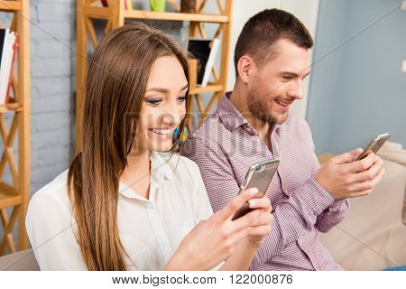 Two happy lovers with mobile phones typing messages